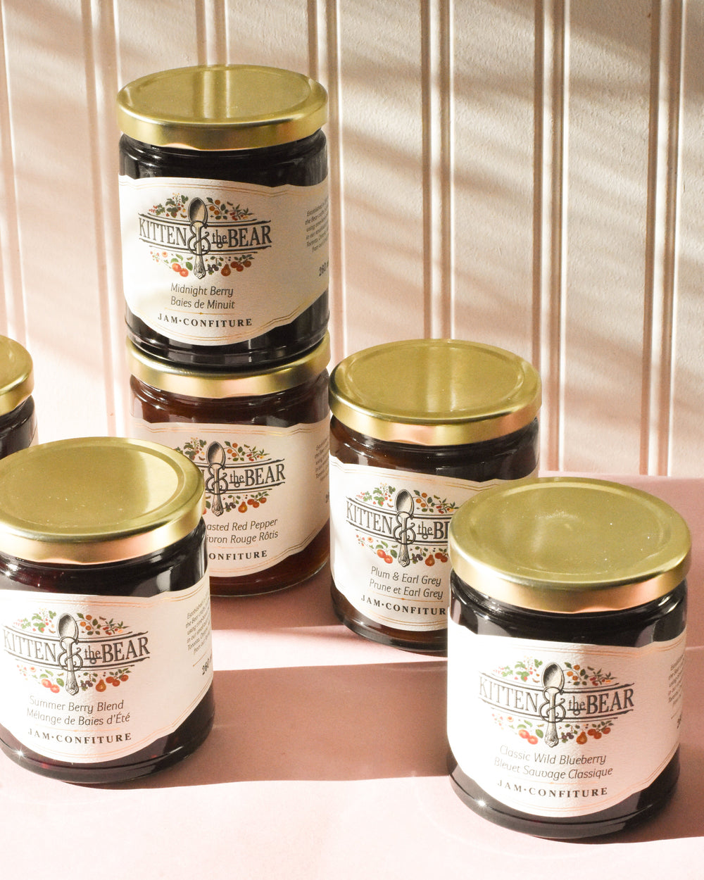 Jars of jam with gold lids on a pink and white striped background